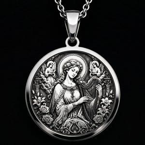 Può includere: Un ciondolo circolare color argento con un rilievo dettagliato di una figura che suona l'arpa, circondata da due angeli alati, motivi floreali e un'aureola. Il ciondolo è appeso a una collana a catena in metallo color argento abbinata.