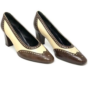 May include: A pair of two-tone, brown and cream-coloured women's heels. The shoes have a classic design with a pointed toe and a block heel. The cream-coloured sections are accented with small, white dots.