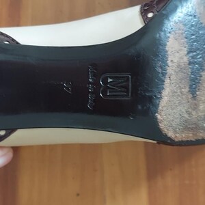 May include: Close-up of a beige and brown women's shoe. The shoe has a black sole with the text "Made in Italy" and the number "37". The shoe has a small heel and a brown leather accent.