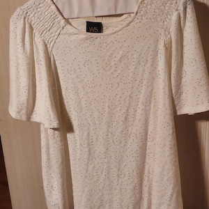 May include: Cream-coloured, long-sleeved top with a round neckline and short, flared sleeves. The fabric is textured with small, evenly spaced holes. The top has a gathered detail at the shoulders and the label "W5" is visible.