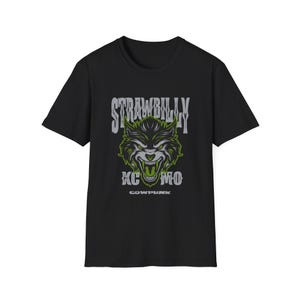 May include: Black t-shirt featuring a wolf graphic with green and gray accents. The text "STRAWBILLY" arches above the wolf's head, with "KC MO" below. The word "COWPUNK" is printed at the bottom of the design.