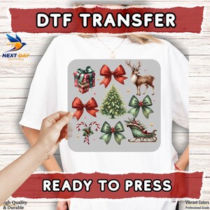 May include: A white t-shirt with a DTF transfer design featuring Christmas elements like bows, a deer, a Christmas tree, and a sleigh. The words "DTF TRANSFER" and "READY TO PRESS" are displayed.
