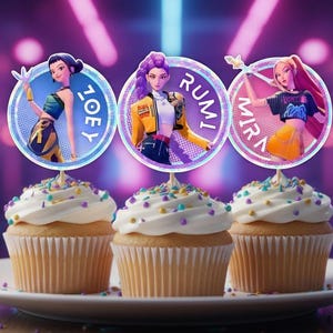 Könnte beinhalten: Drei Cupcakes mit weißem Zuckerguss und bunten Streuseln auf einem weißen Teller. Jeder Cupcake hat einen runden Aufsatz mit einer Cartoonfigur und einem Namen: Joey, Rumi und Mira. Der Hintergrund ist verschwommen, lila und rosa.