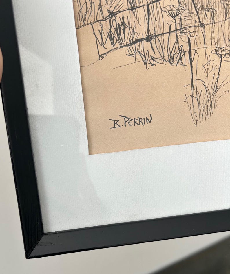 May include: A framed pen and ink drawing featuring a landscape scene with tall grasses and a fence. The artwork is signed "B. Perrin" in the lower right corner. The drawing is set against a tan background and framed in a black frame with a white mat.