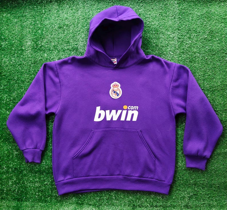 May include: A purple hooded sweatshirt with a front pocket and a white "bwin.com" logo. The sweatshirt features a team crest and is set against a green background.
