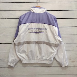 May include: A white and light purple windbreaker jacket featuring a high collar, long sleeves with elastic cuffs, and a cinched elastic hem. The back displays embroidered text reading courr&egrave;ges sport futur paris above a horizontal grey stripe.
