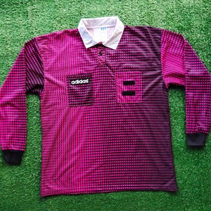 May include: A long-sleeve athletic shirt featuring a gradient pattern of magenta and black squares. The shirt has a white collar, a button placket, and two chest pockets. The word adidas is printed in white on a black patch on the left pocket.