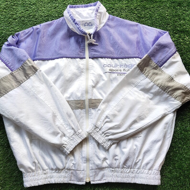 May include: A white and light purple windbreaker jacket with a full-length front zipper, a high collar, and elasticized cuffs and hem. The jacket features grey horizontal stripes on the sleeves and the text Courr&egrave;ges sport futur paris.