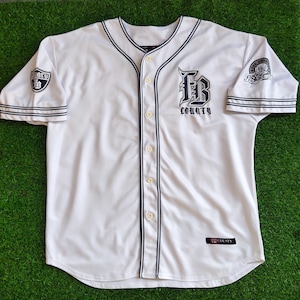 May include: White baseball jersey with navy blue trim and a button-up front. The jersey features the text "FB COUNTY" in navy blue on the chest and sleeves. It has short sleeves and is displayed on a green surface.