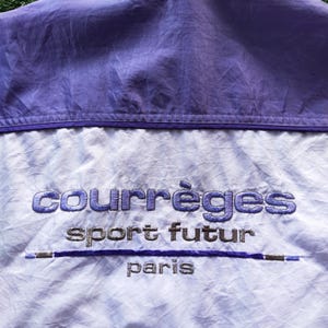 May include: A light purple and white windbreaker jacket featuring the embroidered text courr&egrave;ges sport futur paris in purple and silver thread. The garment has a horizontal purple line accent and a solid purple panel across the upper section.