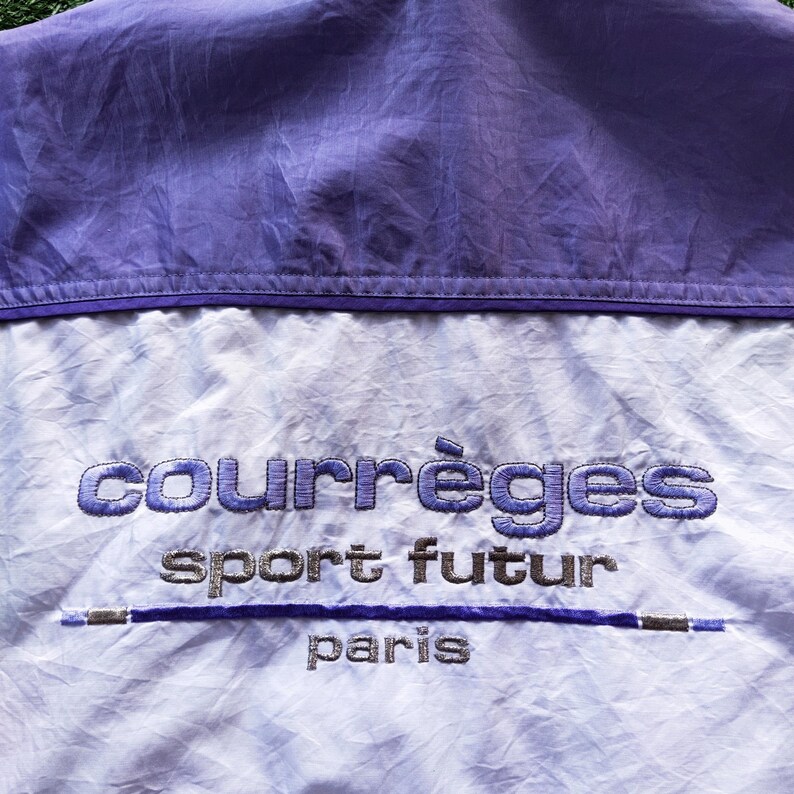 May include: A light purple and white windbreaker jacket featuring the embroidered text courr&egrave;ges sport futur paris in purple and silver thread. The garment has a horizontal purple line accent and a solid purple panel across the upper section.