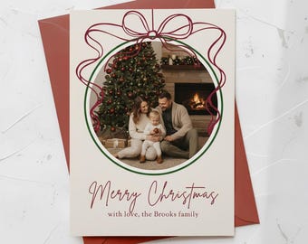 Könnte beinhalten: Weihnachtskarte mit einem Familienfoto in einem grünen Kreis, verziert mit einem bordeauxfarbenen Banddesign. Die Karte trägt die Aufschrift "Merry Christmas" und den Familiennamen. Die Karte liegt auf einem bordeauxfarbenen Umschlag.