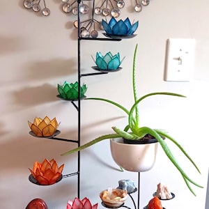 May include: A black metal plant stand with colorful lotus flower candle holders and a potted aloe vera plant. The stand also holds small decorative stones and a bundle of sage. A decorative wall hanging is above the stand.