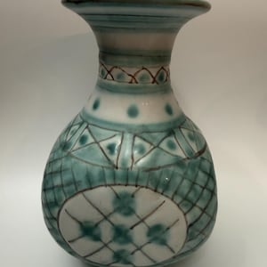 May include: A ceramic vase with a bulbous body and a flared rim, featuring a white base decorated with hand-painted teal blue geometric patterns, including cross-hatching, dots, and circular motifs outlined in thin brown lines.