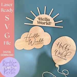 May include: Wooden laser-cut decorations shaped like a sun, cloud, and balloon. The sun reads "Hello World!" and the cloud and balloon say "Hello World, I'm New Here". The image also includes text that says "Laser Ready SVG File DIGITAL DOWNLOAD".