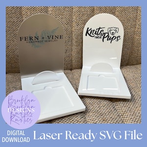 May include: Two white display stands with arched tops. One has "FERN + VINE HANDMADE JEWELRY" text and a botanical design. The other has "Knits and Pups" text and a dog illustration. The stands are labeled "Laser Ready SVG File" and "Digital Download".