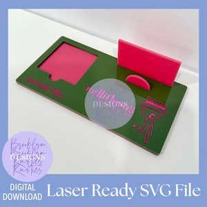 Op de afbeelding: Een laserklare SVG-bestand met een groene basis en roze accenten. Het bevat een roze inzetstuk, een rechthoekig stuk en een halve cirkel. Het ontwerp bevat de tekst "TAP HERE" en een afbeelding van een vrouw die een taart vasthoudt.