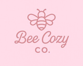 May include: A pink background with a line drawing of a bee above the words "Bee Cozy Co." in a cursive font. The bee is outlined in a darker pink, with details such as wings and stripes. The text is also in a darker pink.