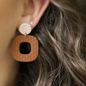 May include: A pair of brown and white woven earrings with a square shape. The earrings are made of a textured material and have a geometric design.