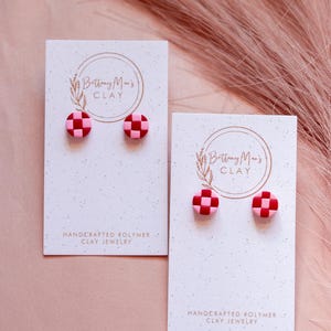 Puede incluir: Dos pares de pendientes de arcilla polimérica a cuadros rosa y rojo en tarjetas blancas con el texto "Brittany Mae's Clay" y "Joyería de arcilla polimérica hecha a mano".