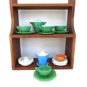 May include: A vintage children's tea set with green, blue, and white cups and saucers, a teapot, and a sugar bowl, displayed on a wooden shelf.