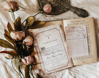 May include: A vintage-themed wedding invitation with the text "TO HAVE AND TO HOLD" and a "BORROWER'S CARD" rests on an open book. Pink flowers and a decorative mirror are also in the image. The invitation includes the names Aubrey Anna Farlton and Isaac Wayne King.