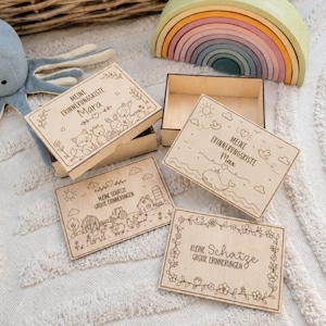 May include: Four rectangular wooden boxes with lids featuring laser-engraved illustrations and text. The designs include woodland animals, a farm scene, a whale, and floral borders. Text includes "Meine Erinnerungskiste," "Max," "Mara," and "Kleine Schätze."