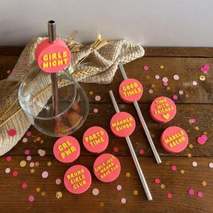 May include: A set of silver metal drinking straws featuring round pink toppers with yellow embossed text including GIRLS NIGHT, GOOD TIMES, TIME WITH FRIENDS, GRL PWR, PARTY TIME, MÄNNER RUNDE, GIRLS JUST WANNA HAVE FUN, DRUNK GIRLS CLUB, and MÄDELS ABEND.