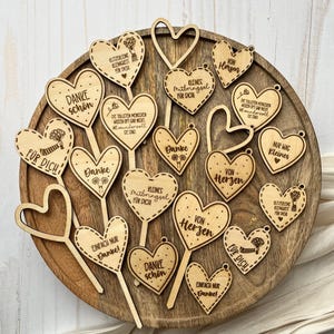 May include: A collection of wooden heart-shaped decorations with various German phrases, including "Danke schön" and "Für dich." The hearts are arranged on a wooden tray, showcasing a natural wood grain. Some hearts have stems.
