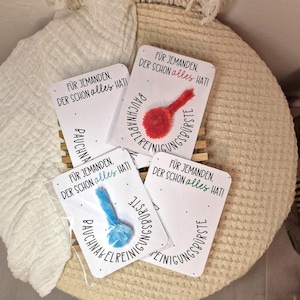 Könnte beinhalten: Vier kleine Karten mit dem Text "FÜR JEMANDEN, DER SCHON alles HAT!" und einem kleinen, flauschigen Objekt. Die Objekte sind rot und blau. Die Karten liegen auf einer gewebten Oberfläche.