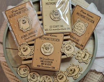 May include: A collection of wooden monster-themed pins and cards. The pins feature various cartoon monster designs. The cards have text in German, including "Mein kleines MUTMONSTERCHEN" and "KLEINER, GRUSELIGER Glücksbringer."