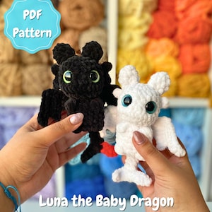 May include: Two crocheted baby dragon toys, one black and one white, are displayed against a backdrop of colourful yarn. The black dragon has green eyes, while the white dragon has blue eyes. The text "PDF Pattern" and "Luna the Baby Dragon" are visible.