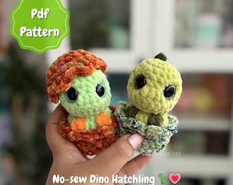 May include: Two crocheted dinosaur hatchlings in their eggs. One is green with an orange head, the other is light green. The image includes the text "Pdf Pattern" and "No-sew Dino Hatchling".