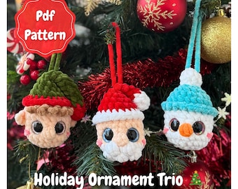 May include: A trio of handmade crochet holiday ornaments. The ornaments include a green elf, a red Santa, and a blue snowman. Each ornament has large, expressive eyes and is suspended from a Christmas tree. The text "Holiday Ornament Trio" is visible.