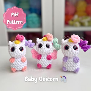 Op de afbeelding: Drie handgemaakte gehaakte baby eenhoorn speelgoed. Elke eenhoorn is wit met grote zwarte ogen, kleurrijke manen en kleine vleugels. De afbeelding bevat de tekst "Pdf Pattern" en "Baby Unicorn".