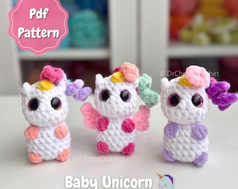 May include: Three handmade crochet baby unicorn toys. Each unicorn is white with large black eyes, colorful manes, and small wings. The image includes the text "Pdf Pattern" and "Baby Unicorn".