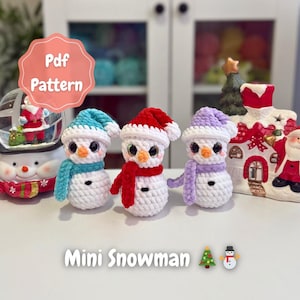 Puede incluir: Tres mini muñecos de nieve de ganchillo con sombreros y bufandas azules, rojas y moradas. Cada muñeco de nieve tiene ojos negros y una nariz naranja. La imagen incluye el texto "Mini Muñeco de Nieve" y "PDF Pattern".
