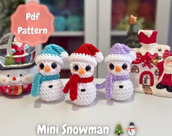 May include: Three crocheted mini snowmen with blue, red, and purple hats and scarves. Each snowman has black eyes and an orange nose. The image includes the text "Mini Snowman" and "PDF Pattern".