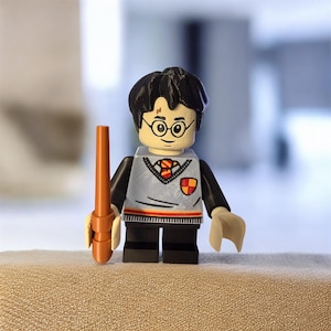 May include: A Lego-style figurine of a character with black hair, round glasses, and a lightning bolt scar. The figure wears a grey sweater vest over a white shirt, black trousers, and holds a brown wand. The figure has a red and gold crest on the chest.