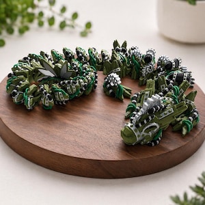 Può includere: Una collezione di oggetti decorativi verdi e argentati, simili a creature stilizzate, disposti su un vassoio rotondo di legno. Gli oggetti presentano dettagli intricati e sono accentuati da elementi in bianco e nero.