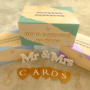 Puede incluir: Una caja de recuerdos de boda de madera con un diseño pintado en verde azulado y beige, personalizada con nombres y una fecha. Incluye cajas de tarjetas a juego y letreros de Sr. y Sra.