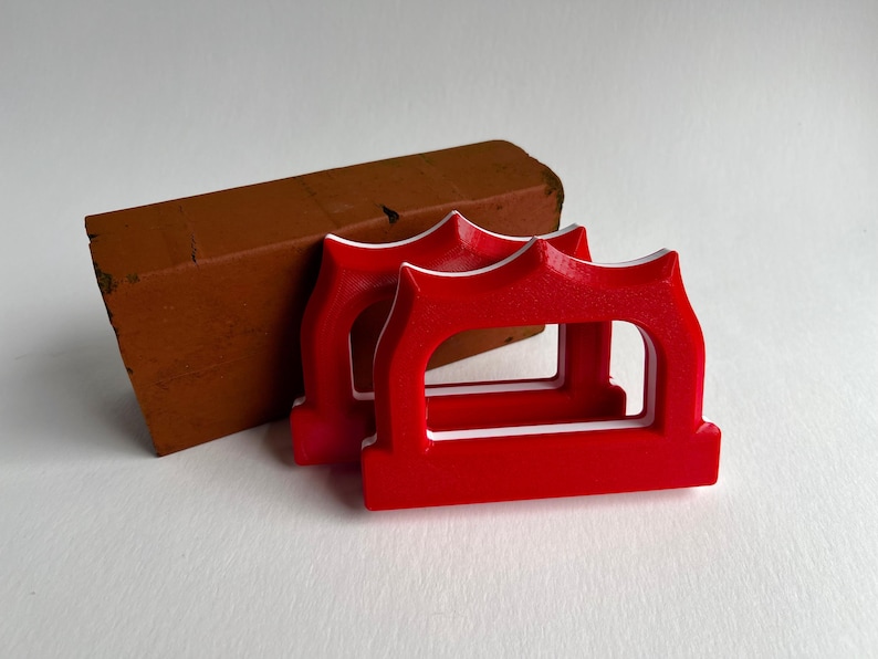 May include: Two bright red, arched-shaped objects with white trim are in the foreground, next to a brown brick. The objects have a decorative top and a rectangular opening. The brick is a reddish-brown color.