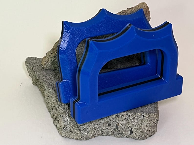 May include: Two blue decorative objects with a black trim, resting on a piece of gray stone. The objects have a unique arched design. The background is a plain white surface.