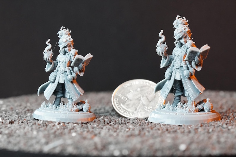 May include: Two unpainted gray resin miniature figures of a spellcaster wearing a long coat, goggles, and boots. Each figure holds an open book in one hand and a flame effect in the other, standing on a circular base next to a US quarter coin.