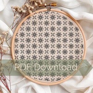 May include: A round embroidery hoop with a beige fabric featuring a repeating black floral pattern. The wooden hoop is secured with a brass screw. The text "PDF Download" is visible on the lower portion of the image. Dried flowers are in the background.