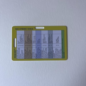 May include: A yellow card with the text "NIH STROKE SCALE" at the top. The card has a hole at the top for hanging and contains detailed medical information, including scales for motor function, language, and sensory perception.