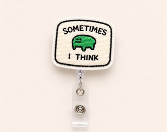 May include: A badge reel featuring a rectangular off-white embroidered patch with black stitched borders. The patch displays the black text "SOMETIMES" above a small green creature illustration and the black text "I THINK" below the creature.
