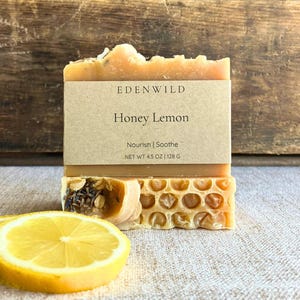 Puede incluir: Una pastilla de jabón Honey Lemon con una etiqueta que dice "EDENWILD" y "Honey Lemon". El jabón es de color marrón claro con un diseño de panal y una rodaja de limón. Peso neto 128 g.