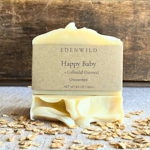 May include: A bar of unscented soap with the text "Happy Baby + Colloidal Oatmeal" on a brown label. The soap is light yellow and sits on a surface with scattered oats. The soap weighs 4.5 oz.