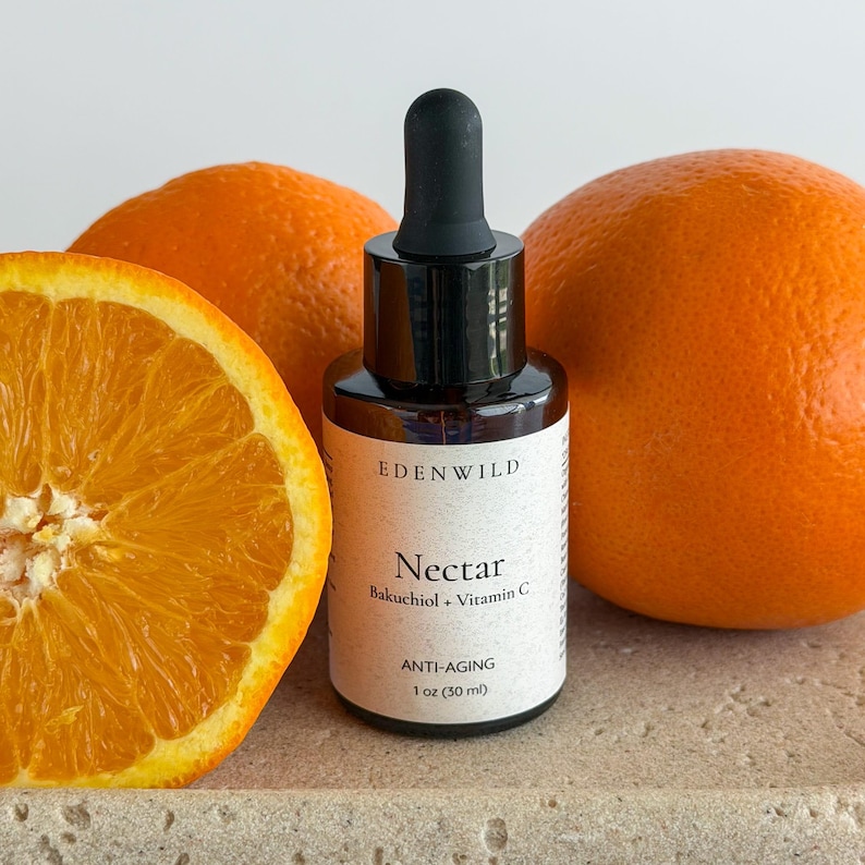 May include: A skincare product bottle labeled "Nectar" with "Bakuchiol + Vitamin C" and "ANTI-AGING" text, next to two whole oranges and a sliced orange. The bottle is 1 oz (30 ml).